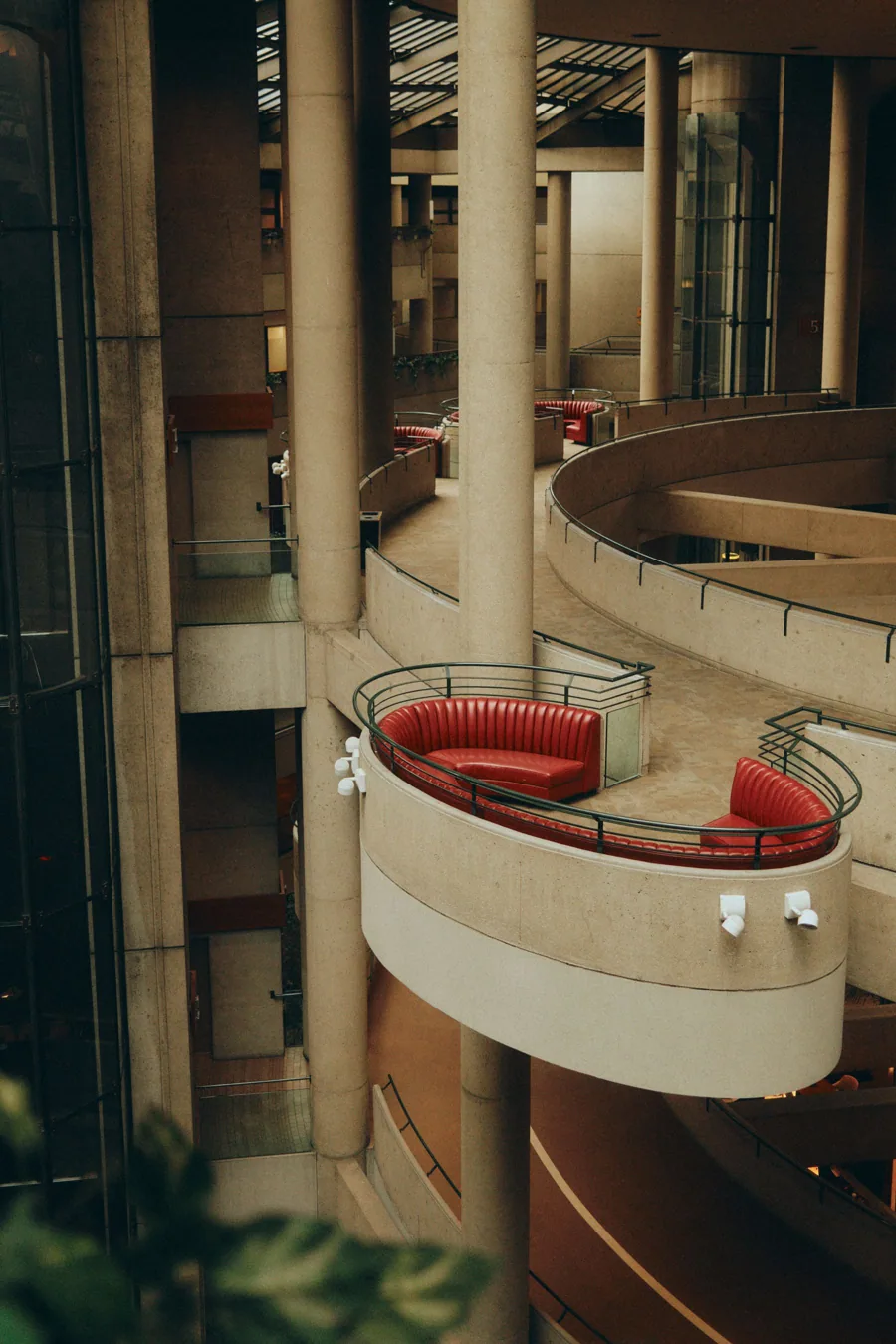 Interior de galerías curvas de hormigón con barandillas y asientos tapizados en rojo.