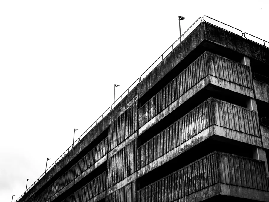 Esquina de un edificio de hormigón en alto contraste sobre cielo blanco.
